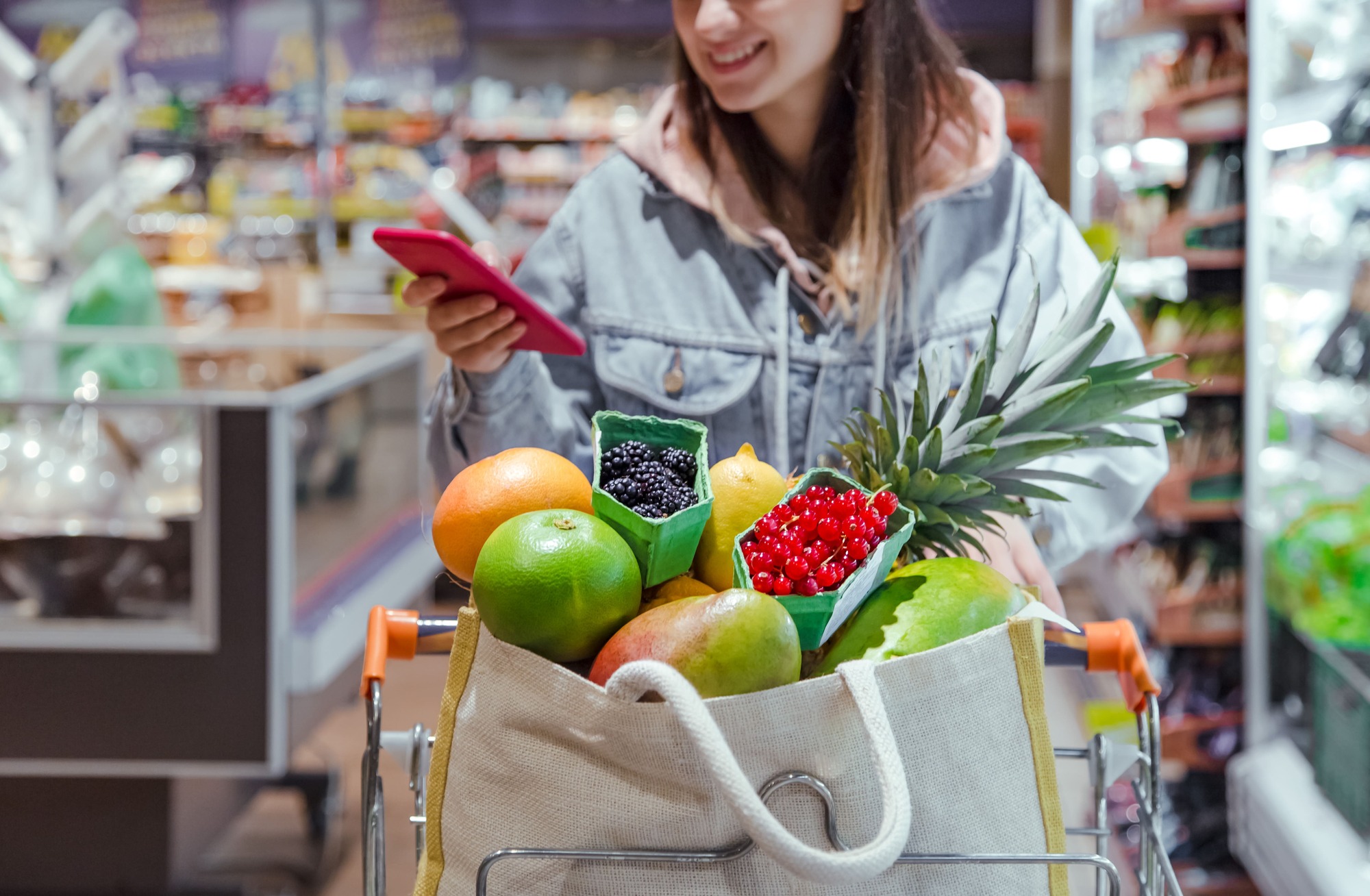 een-jong-vrouw-winkelt-voor-eten-in-een-supermarkt-met-een-telefoon-in-de-hand voedsel kopen op Aruba